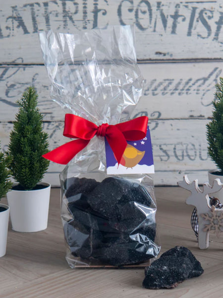 Christmas Coal Cinder Toffee packaged in a clear bag tied with a red ribbon on a Christmassy background.