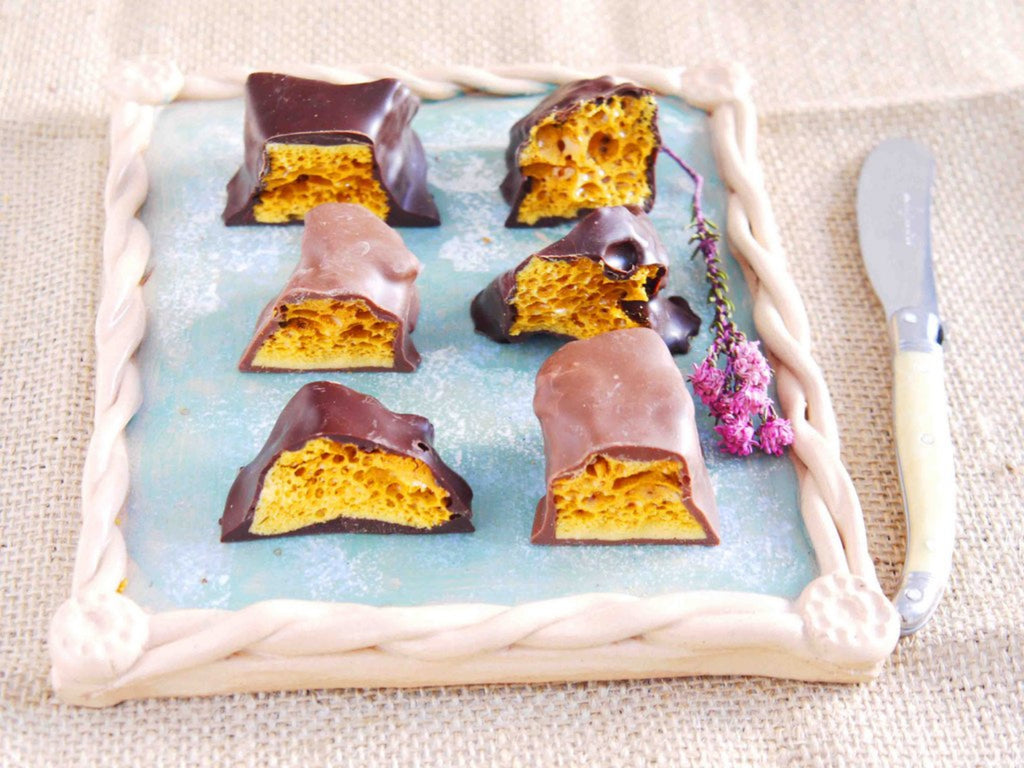 Chunks of milk chocolate and dark chocolate cinder toffee on a plate. Each piece is cut in half to show the cinder toffee inside.
