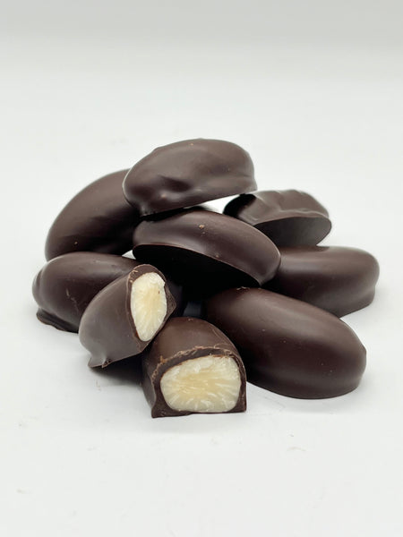 Pile of brazil nuts dipped in dark chocolate on a white background. One nut cut in half to reveal the inside.
