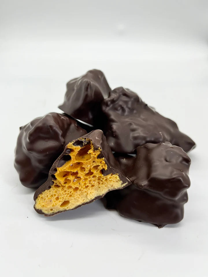 Chunks of cinder toffee dipped in dark chocolate. One piece is cut open showing the cinder toffee inside.