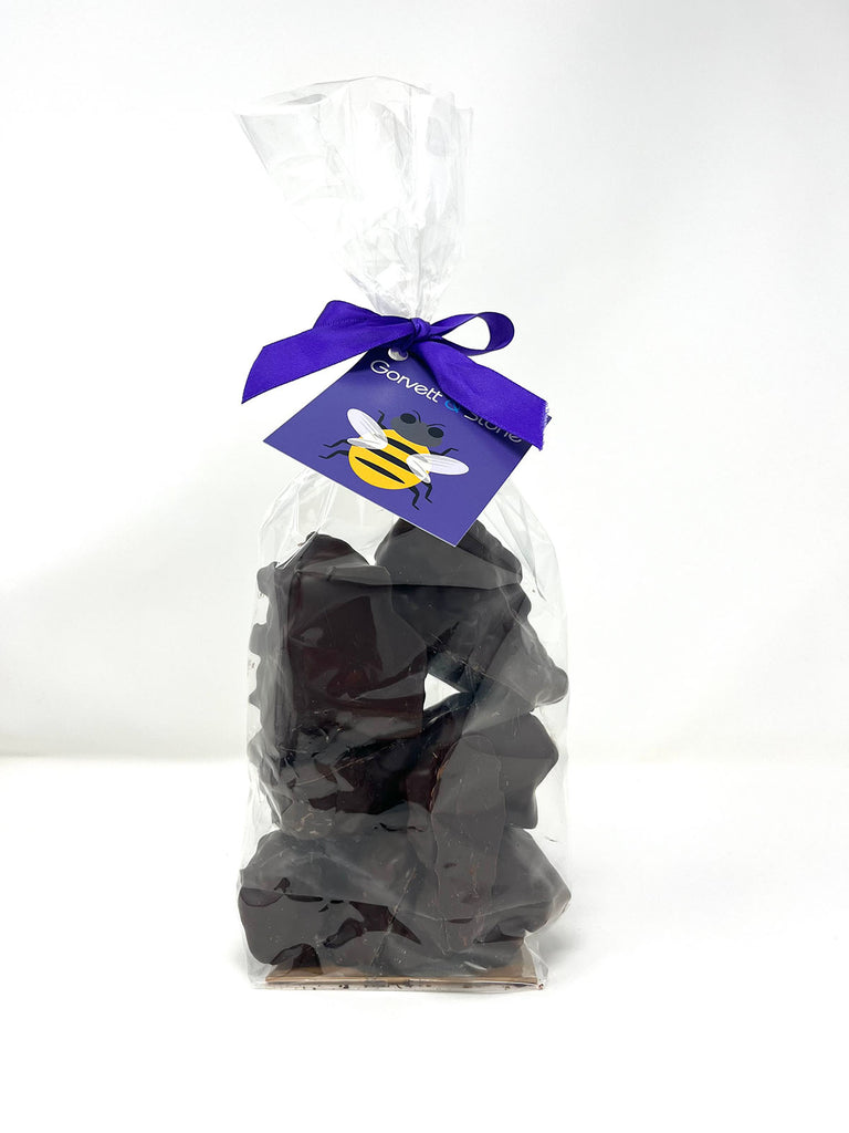 Clear bag filled with dark chocolate cinder toffee. Tied with a ribbon and a tag. On a plain white background.