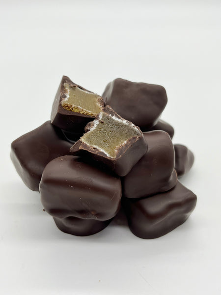 Pile of stem ginger in dark chocolate on a white background. One piece cut open to show the inside.