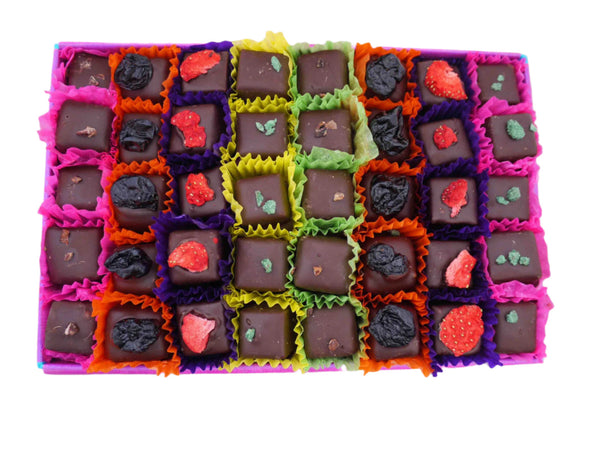 Open gift box of 40 brightly decorated dark chocolates. Each chocolate sits in a colourful petit four case. Viewed from above on a white background.