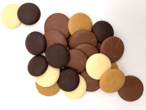 Mixture of milk chocolate, dark chocolate, white chocolate and gold chocolate buttons scattered on a plain white background.