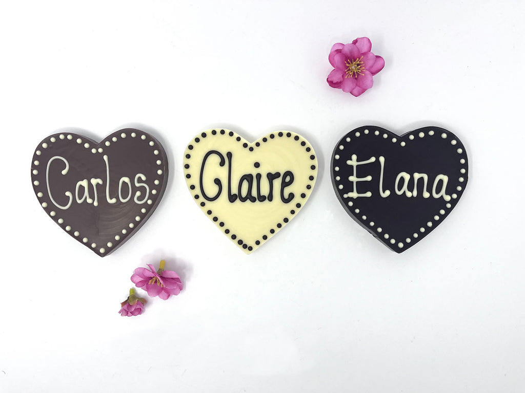 3 chocolate hearts piped with Carlos, Claire and Elana. On a white background with 3 cherry blossom flowers.