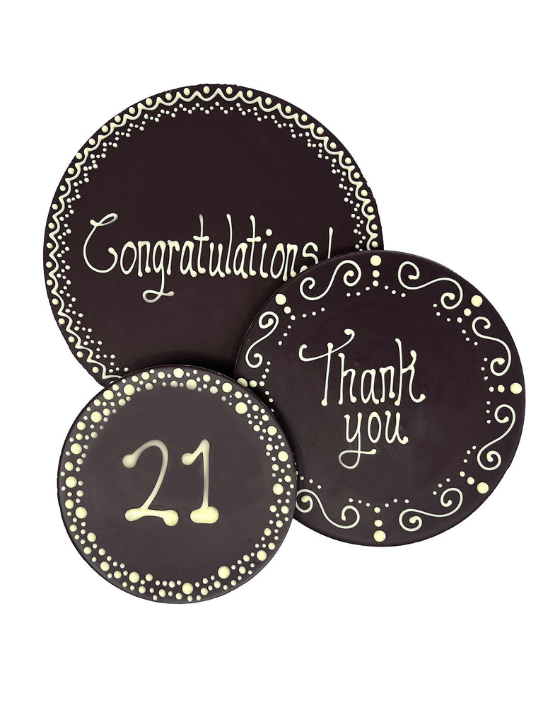 3 Dark chocolate plaques hand piped with decorative borders and '21' 'Congratulations!' and 'Thank you' text in white chocolate. On a white background.