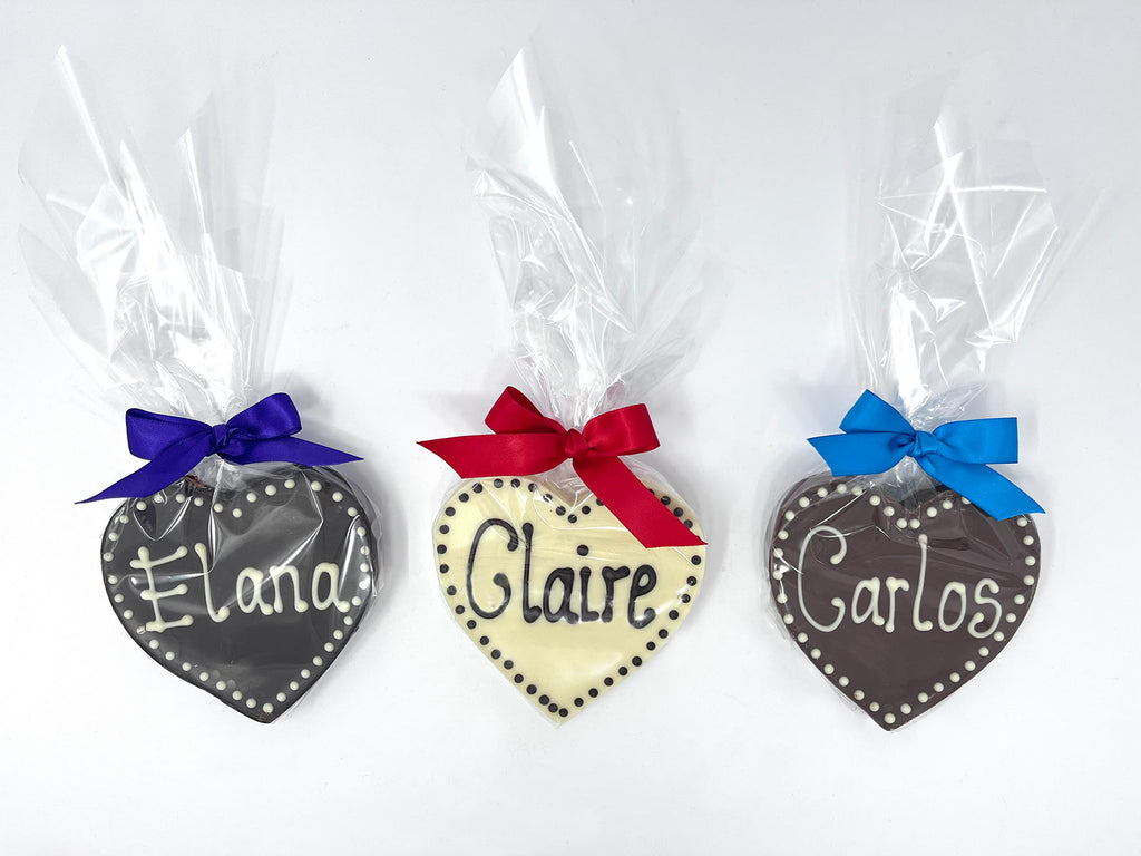 3 chocolate  hearts with names piped. Wrapped in cellophane and tied with satin ribbons. On a white background.