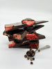 A stack of dark chocolate shards infused with black pepper, studded with freeze-dried strawberries, and accompanied by a spoonful of black peppercorns.