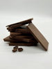 Stack of milk chocolate shards with 3 coffee beans in front. On a white background.