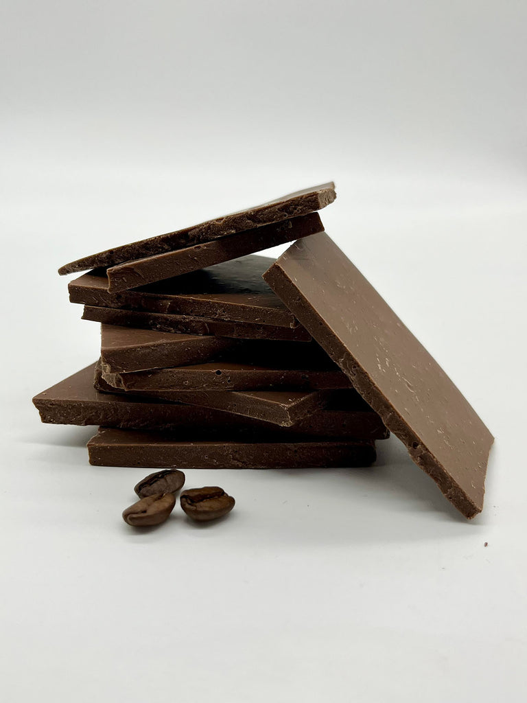 Stack of milk chocolate shards with 3 coffee beans in front. On a white background.