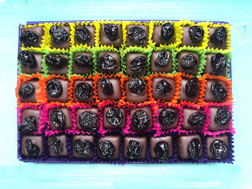 Open gift box of 40 cherry marizipans in dark chocolate. Each one decorated with a whole dried cherry.  