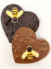 One dark and one milk chocolate honeycomb heart decorated with a white and dark chocolate honeybee. Viewed from above on a white background. 