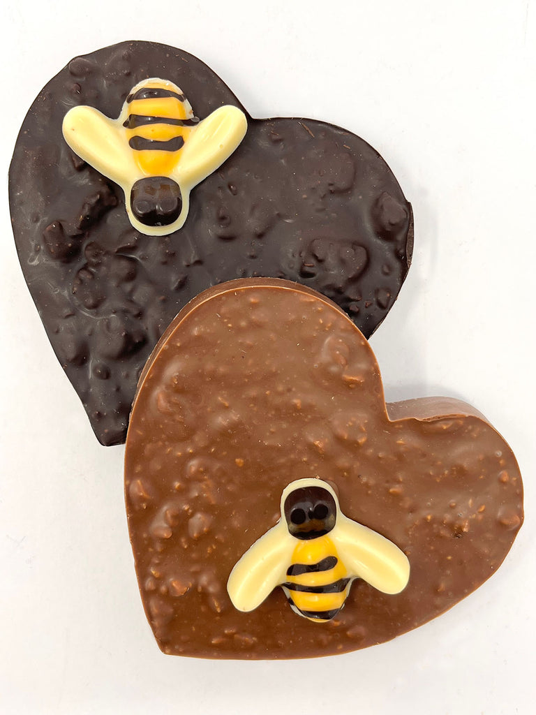 One dark and one milk chocolate honeycomb heart decorated with a white and dark chocolate honeybee. Viewed from above on a white background. 
