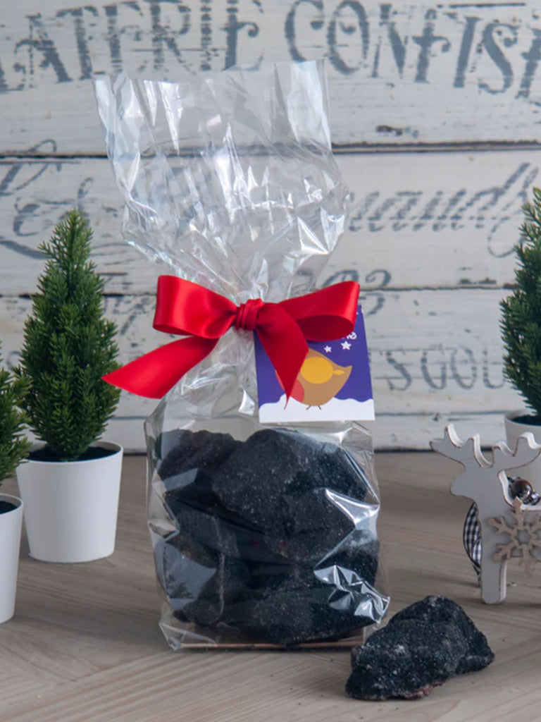 Christmas Coal Cinder Toffee packaged in a clear bag tied with a red ribbon on a Christmassy background.