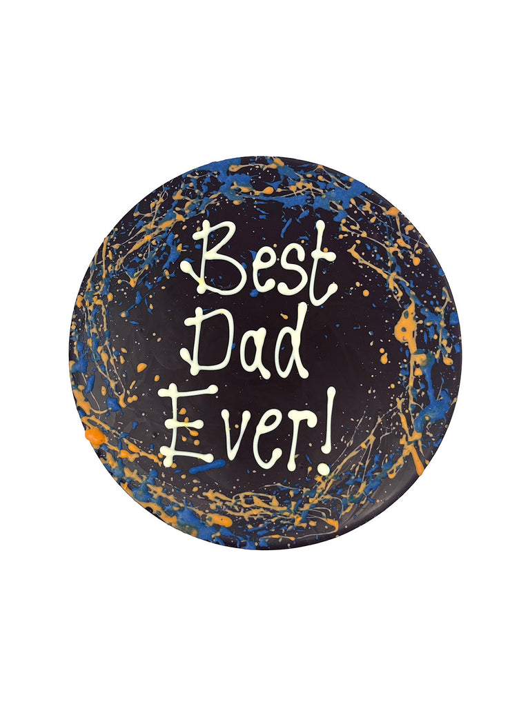 One round dark chocolate father's day plaque. Decorated with blue and orange splashes and piped Best Dad Ever! On a white background.