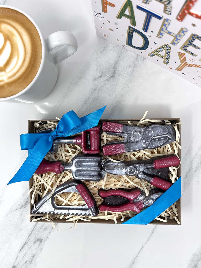 Gift set of dark chocolate miniature garden  tools in a box on a marble surface with a coffee cup and 'Fathers Day' card.