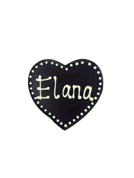 Dark chocolate heart with Elana piped in white chocolate. On a white background.