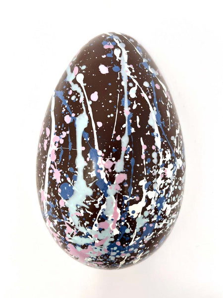 Decorated dark chocolate egg with splatter design on a white background.