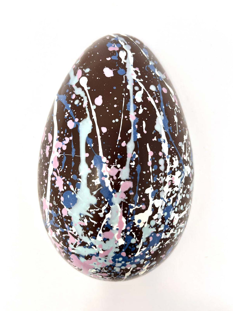 Decorated dark chocolate egg with splatter design on a white background.