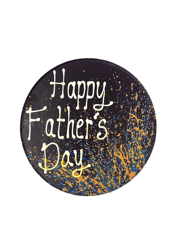 One round dark chocolate father's day plaque. Decorated with blue and orange splashes and piped Happy Father's Day. On a white background.