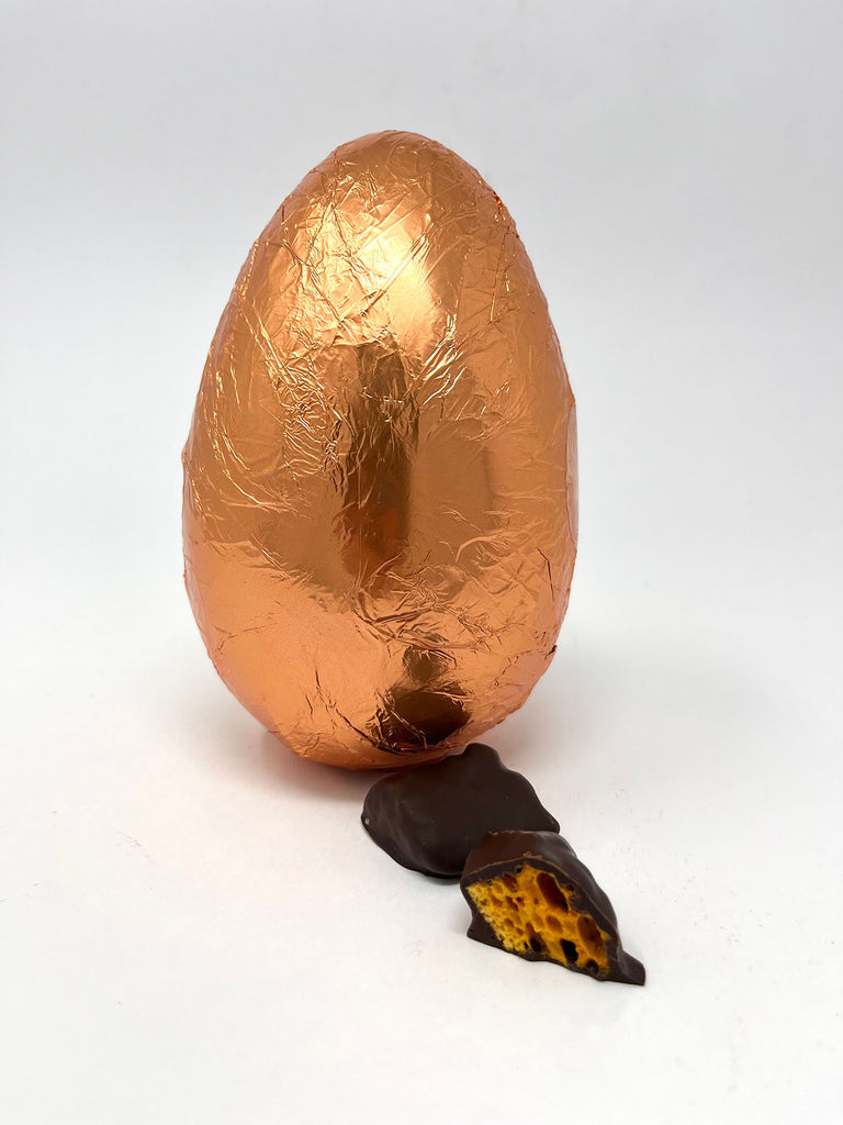 Dark Chocolate Easter Egg in copper foil with two pieces of dark chocolate cinder toffee in the foreground.  On a white background.