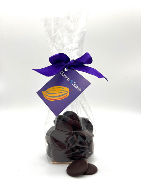 Dark chocolate buttons in a clear bag tied with a ribbon and a tag.  On a white background.