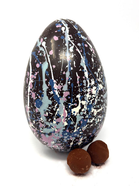 Decorated dark chocolate egg with splatter design and two chocolate truffles on a white background