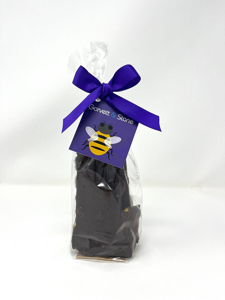 Dark chocolate honeycomb shards packaged in a clear bag tied with a ribbon and a bumble bee tag.  On a white background.