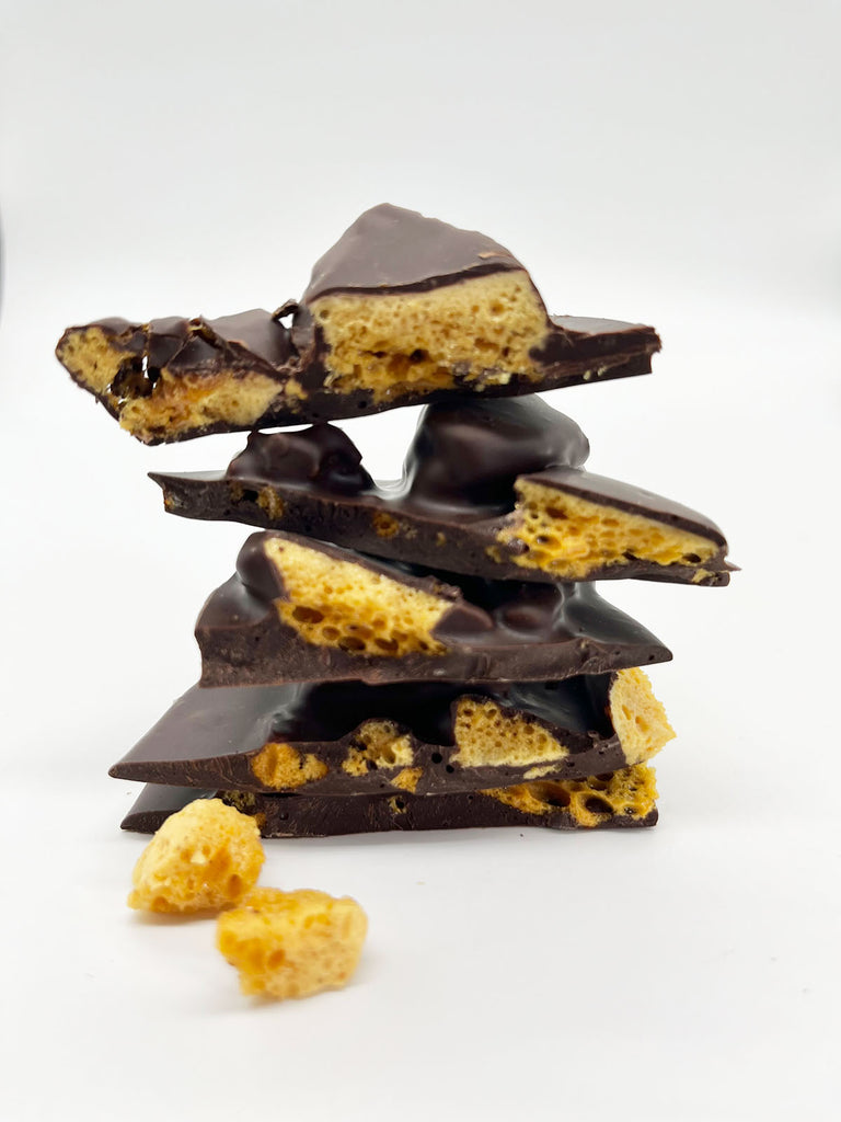 A stack of dark chocolate shards with visible pieces of honeycomb inside, placed against a white background.