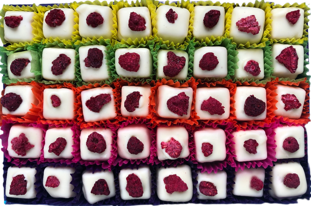 Open gift box of 40 Eton Mess chocolates in white chocolate and topped with a red freeze-dried raspberry. Each chocolate sits in a brightly coloured petit four case. Pictured from above
