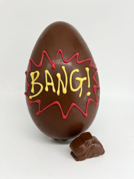 Exploding milk chocolate Easter egg with 'BANG!' piped in red and yellow and a small chocolate bunny on a white background