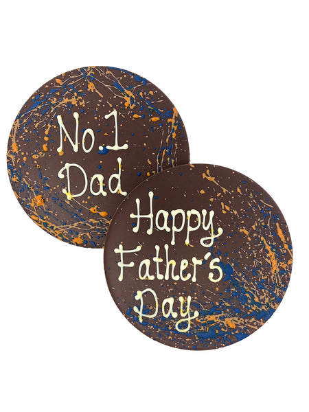 Two round milk chocolate father's day plaques. Decorated with blue and orange splashes and piped No 1 Dad and Happy Father's Day. On a white background.