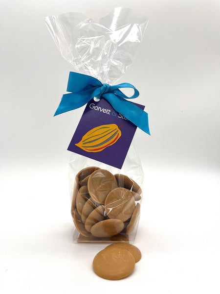 Caramelised white chocolate buttons in a clear cellophane bag tied with a G&S tag and a blue ribbon.  On a white background.