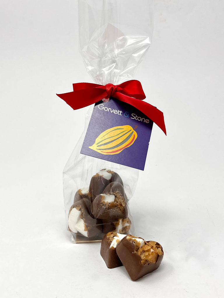 Milk chocolate hearts with fragments on marshmallow and wafer. Packaged in a clear bag tied with a red ribbon. On a white background.