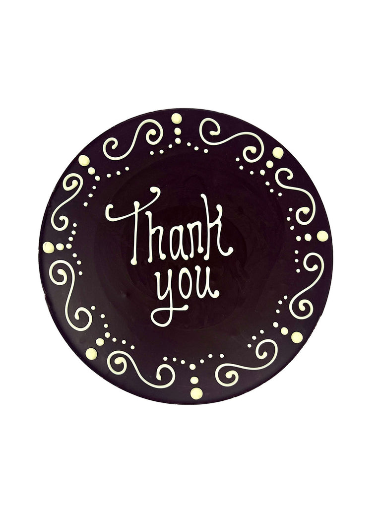 Dark chocolate plaque hand piped  with a decorative border and 'Thank you' text in white chocolate. On a white background.