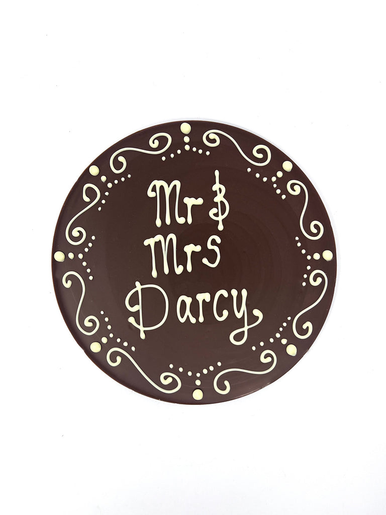 Milk chocolate plaque hand piped  with a decorative border and 'Mr & Mrs Darcy' text in white chocolate. On a white background