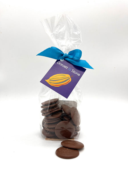 Milk chocolate couverture buttons packaged in a clear cellophane bag. Tied with a blue ribbon and tag. Pictured on a white background.