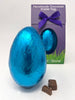 Handmade chocolate Easter egg in blue foil with a purple gift box on a white background
