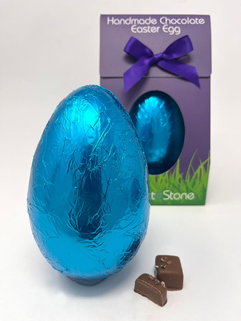 Handmade chocolate Easter egg in blue foil with a purple gift box on a white background