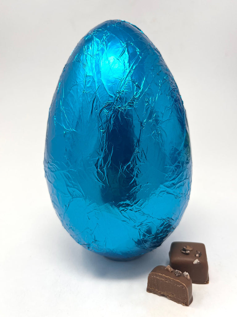 Handmade chocolate Easter egg wrapped in blue foil with two smaller chocolate pieces on a white background