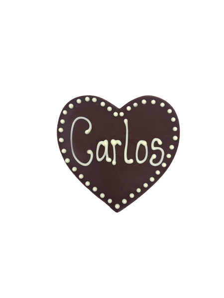 Milk chocolate heart piped with the name Carlos. On a white chocolate background.