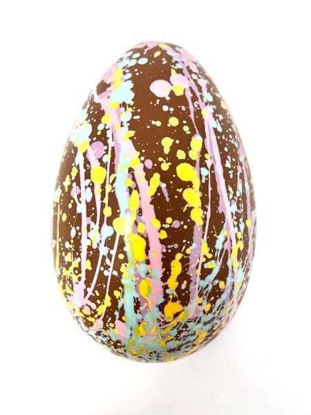 Decorated milk chocolate egg with splatter design on a white background.