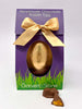 Gold foiled Easter Egg in purple Gorvett and Stone Box tied with a gold ribbon.  On a white background with 2 pieces of Cinder Toffee in the foreground.