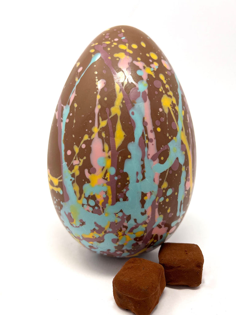 Decorative milk chocolate egg with splatter design and two chocolate truffles on a white background