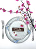 Decorative place setting with a milk chocolate bar as a name card labeled 'Henry', silverware, and cherry blossom branches on a white background.