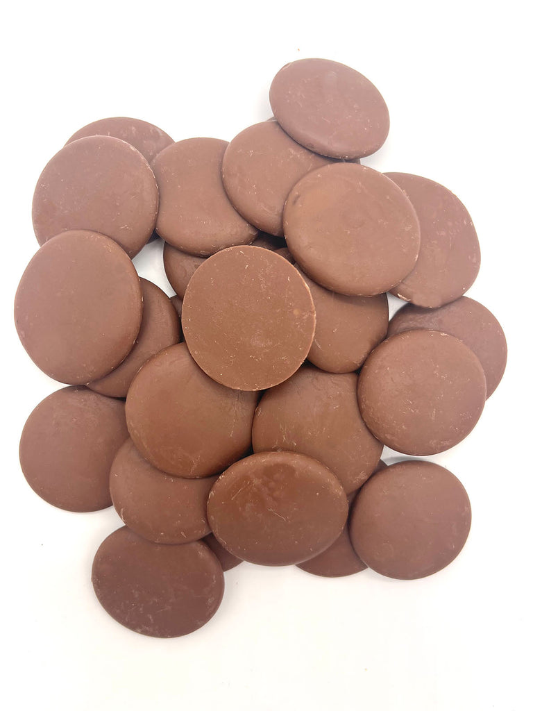 Pile of milk chocolate couverture buttons on a white background.