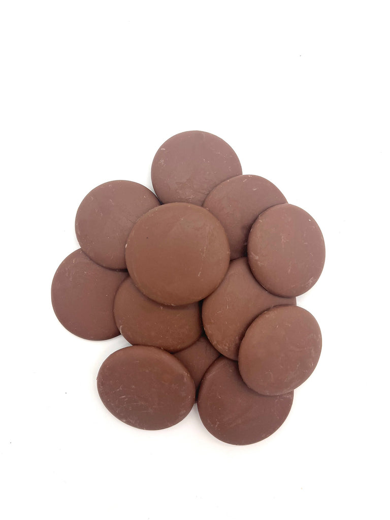 Pile of milk chocolate couverture buttons on a white background.