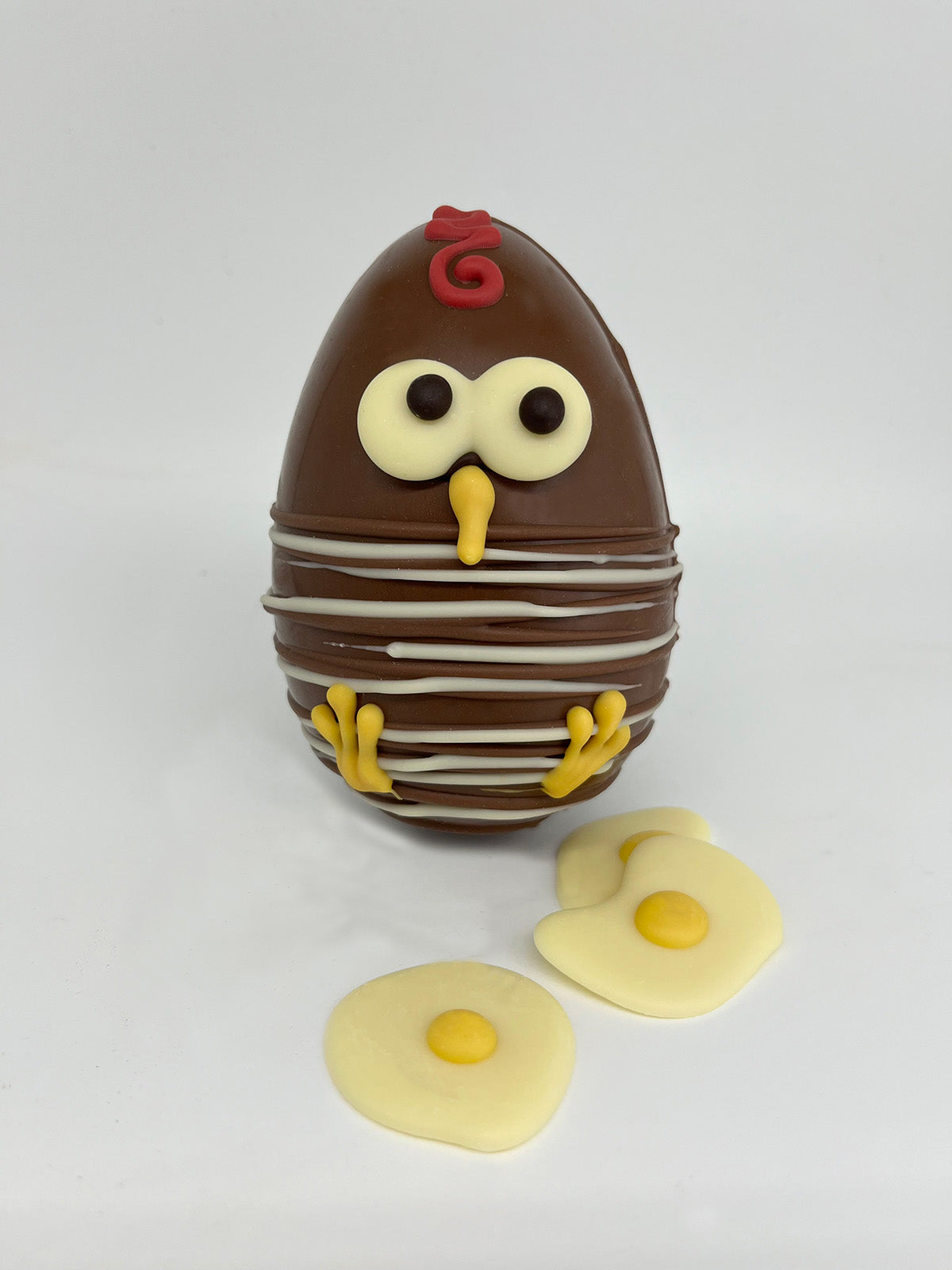 Milk chocolate  Easter Egg with white and dark chocolate chick decoration. 3 white chocolate mini fried eggs in the foreground. On a white background