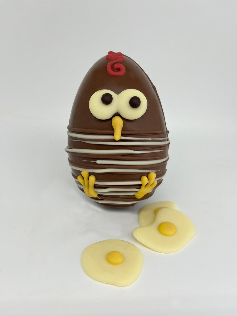 Milk chocolate  Easter Egg with white and dark chocolate chick decoration. 3 white chocolate mini fried eggs in the foreground. On a white background