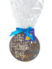 Round milk chocolate plaque decorated with orange and blue splashes and piped Happy Father's Day. Wrapped in cellophane and tied with a blue satin ribbon and gift tag. On a white background.